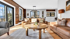 A spacious living room with a large wooden coffee table, leather sofas, and a view of the outdoors. - 3 Min to Slopes  | Stunning Mountain View (Newry)