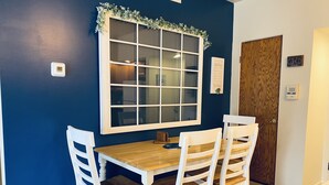 A dining area with a wooden table and white chairs, a window with a white frame, and a door with a wooden panel. - Country Apartment Rental in an Outdoor Paradise! (Mount Carroll)