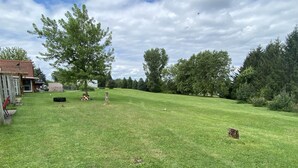 A grassy yard with a wooden deck, a tree, and a white building in the background. - Country Apartment Rental in an Outdoor Paradise! (Mount Carroll)