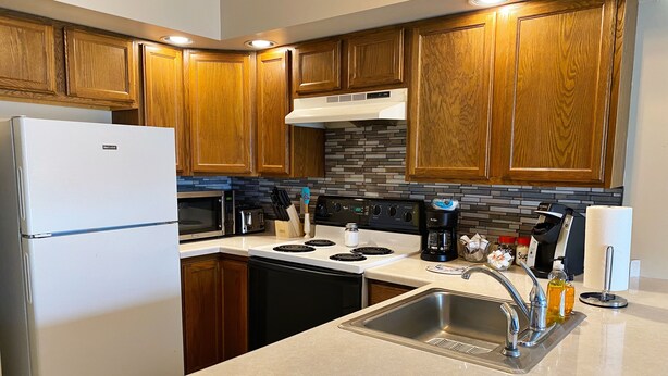 A modern kitchen with wooden cabinets, a stainless steel refrigerator, a microwave, a stove, and a sink. - Country Apartment Rental in an Outdoor Paradise! (Mount Carroll)