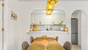 Ein Essbereich mit einem Holztisch, vier Stühlen, einer Pendelleuchte und weißen Schränken im Hintergrund.