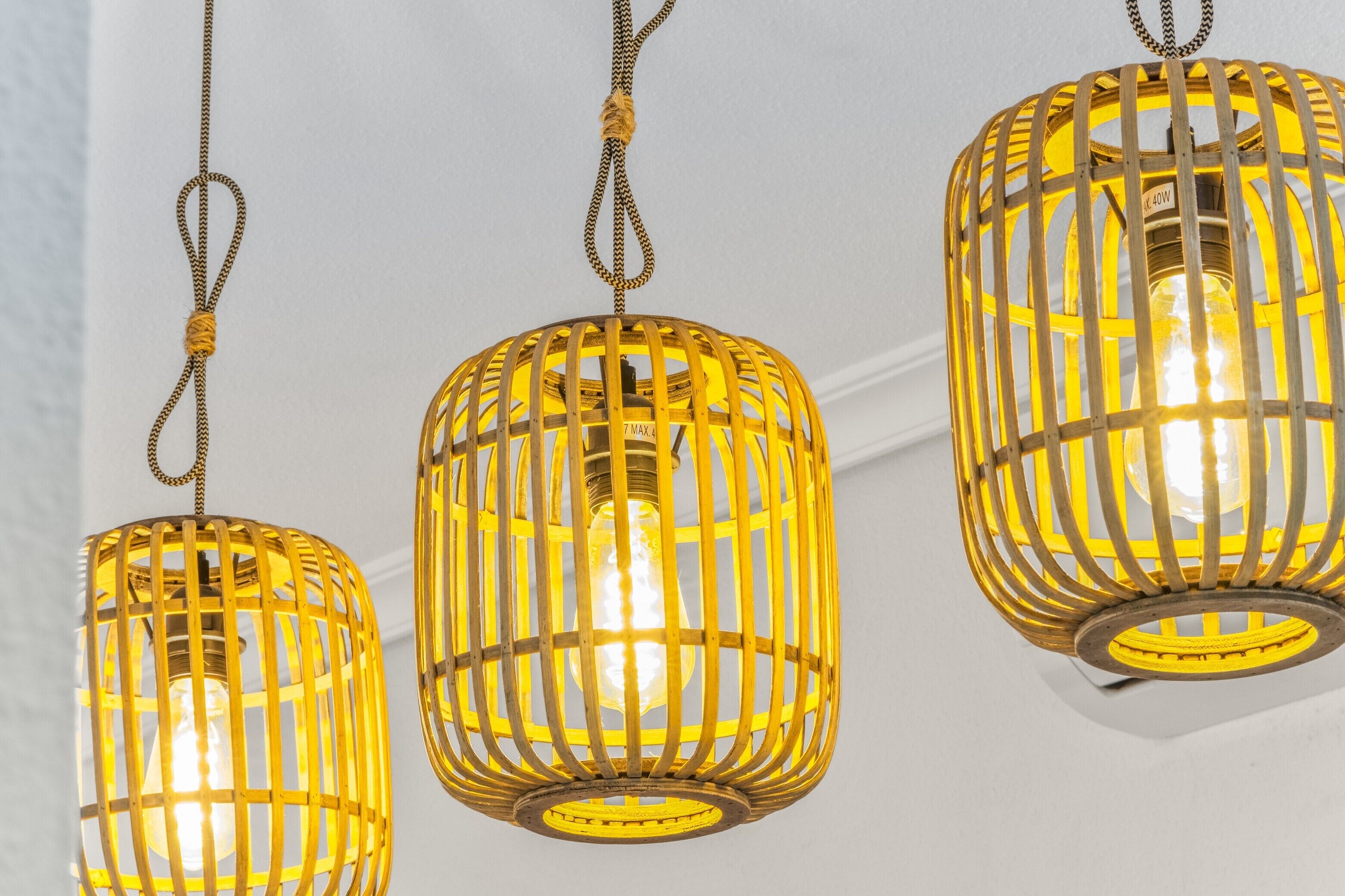 Drie hanglampen met een geelachtige gloed, elk omgeven door een houten rasterwerk.