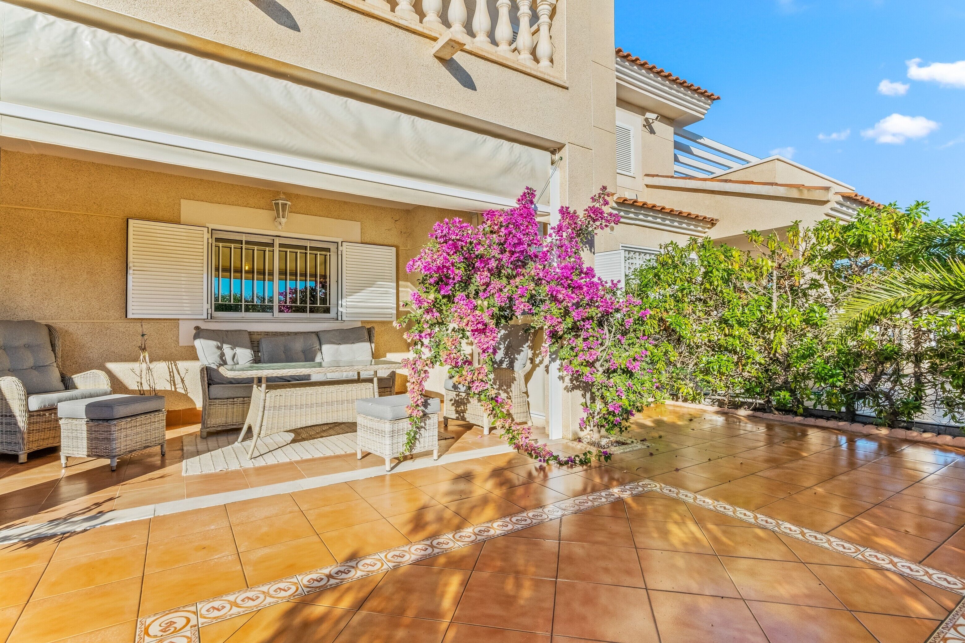 A patio with outdoor furniture, a pergola with flowering plants, and a tiled floor.