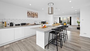Uma cozinha moderna com armários brancos, uma ilha central e banquetas pretas.