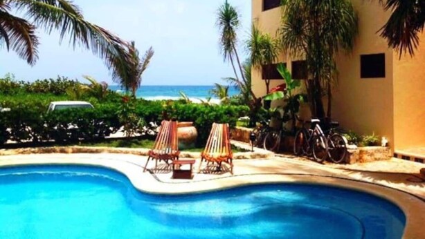 A swimming pool with lounge chairs, a building with a flat roof, and a view of the ocean.