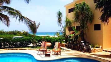 Uma piscina com espreguiçadeiras, um edifício com teto plano e vista para o mar.