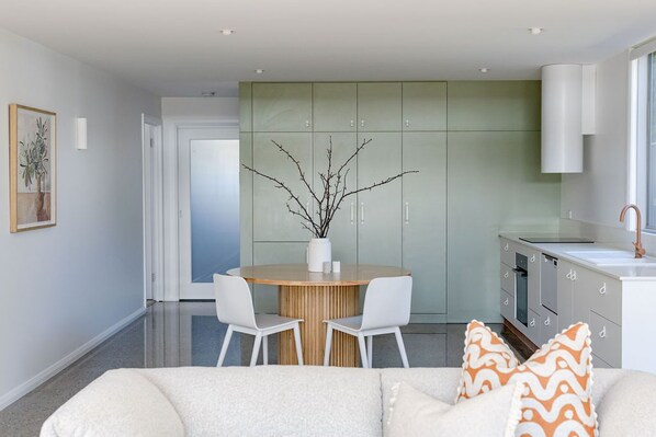 A modern kitchen with a round dining table, white chairs, and a green cabinet.