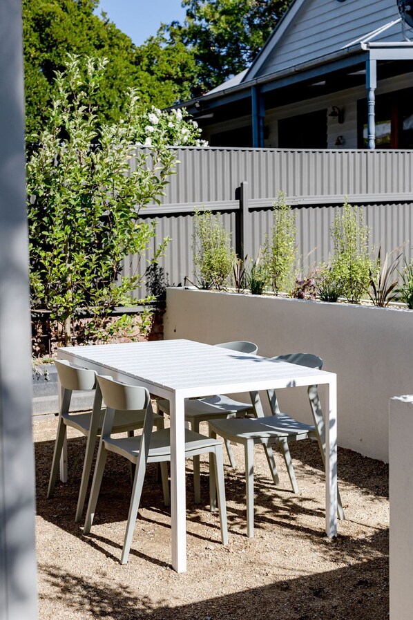 A patio with a white table and chairs, surrounded by a gravel area and plants.