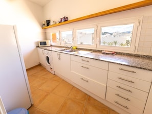 A kitchen with a washing machine, microwave, and a window with a view of buildings.