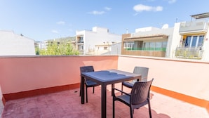 Eine Dachterrasse mit Tisch und Stühlen und Blick auf umliegende Gebäude, unter einem wolkenlosen Himmel.