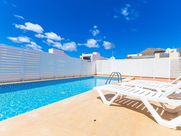 A rooftop pool with clear blue water, white lounge chairs, and a white fence.