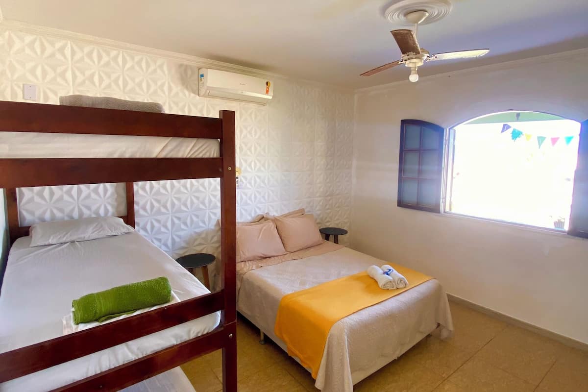 A hotel room with two beds, a ceiling fan, an air conditioning unit, and a window with a view.