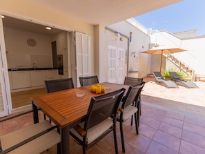 Cozinha e sala de jantar integradas, com uma mesa e cadeiras de madeira, um relógio na parede e uma escada que dá para um andar superior.