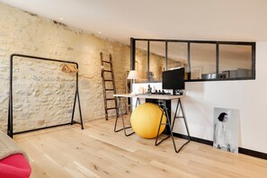Ein Zimmer mit Steinwand, Holzboden, Schreibtisch mit Lampe, gellem Trainingsball, schwarzem Fernseher und Spiegel.