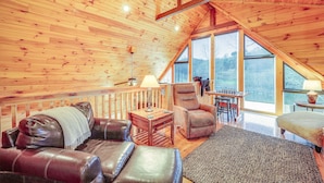 A cozy wooden interior with a leather sofa, a chair, a small table with a lamp, and large windows offering a view of the outdoors. - Waterfront Watauga Lake Home w/ Private Dock! (Butler)