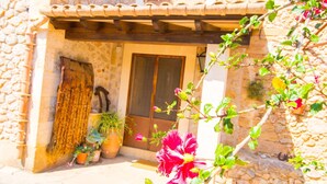Un bâtiment en pierre avec une porte en bois et un toit recouvert de tuiles. On peut voir des plantes en pot et une plante en fleurs au premier plan.