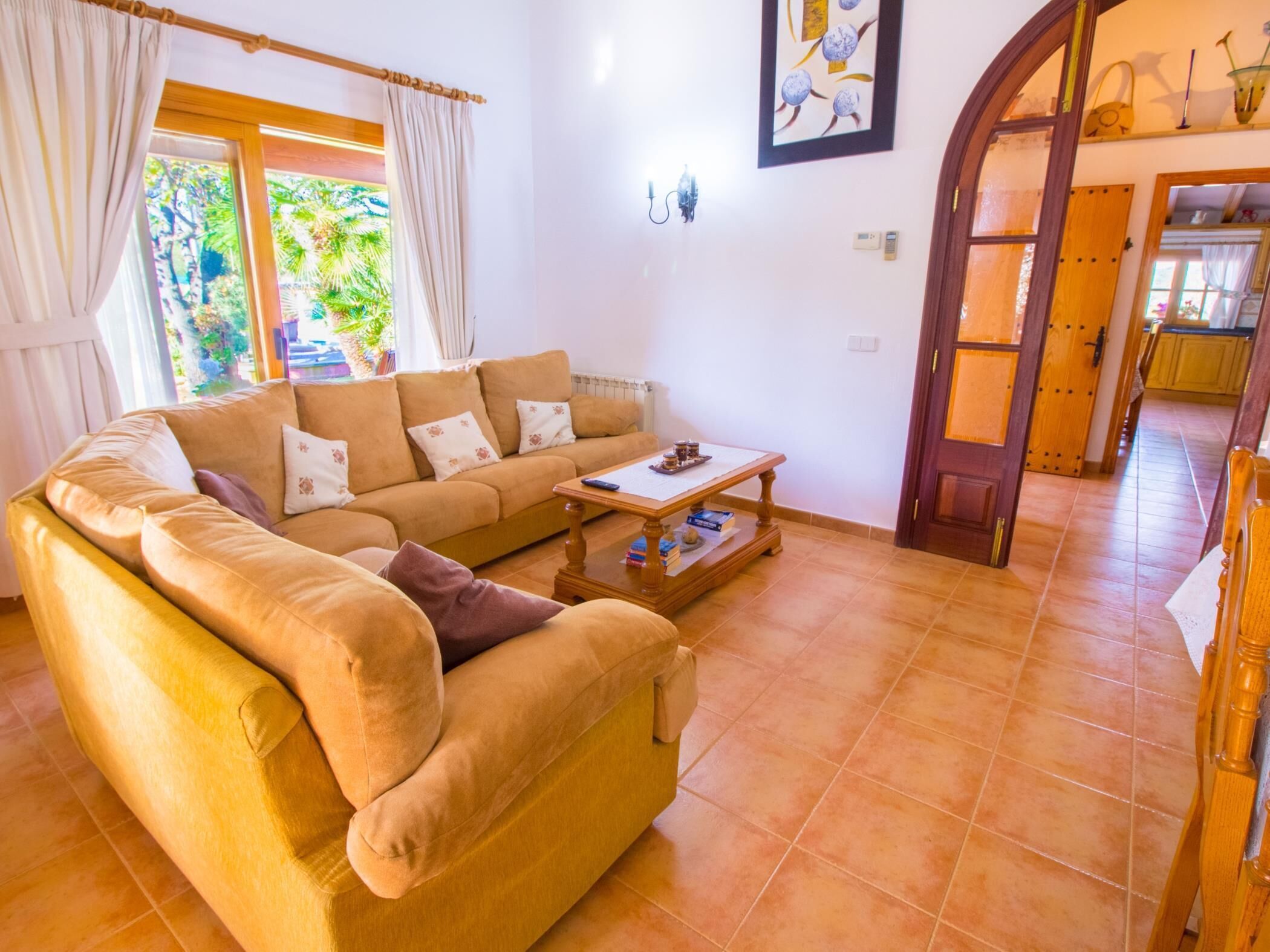 A living room with a beige sofa, a wooden coffee table, and a view of a garden through a window.