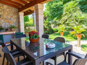 An outdoor patio with a stone wall, a table with chairs, and potted plants. - Sunny villa with private pool, A/C and WIFI (Pollença)