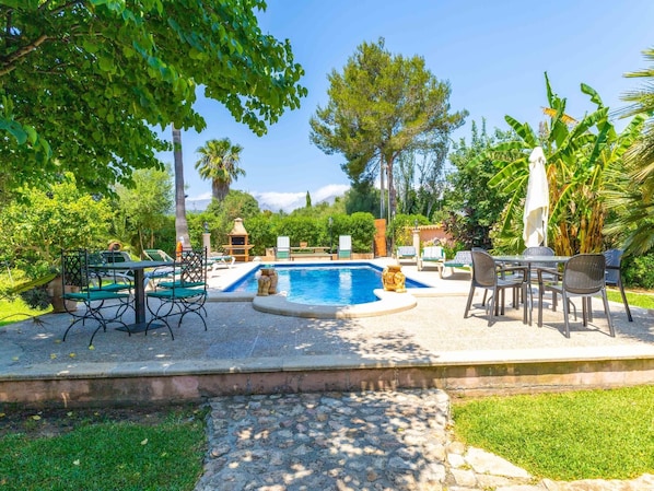 A pool area with lounge chairs, a table, and a barbecue.