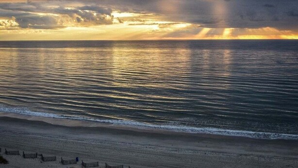 Ein Strand mit ruhiger See und bewölktem Himmel.