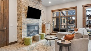 A modern living room with a stone fireplace, large windows, and a cozy seating area. - Blackstone By Lespri Management  (Park City)