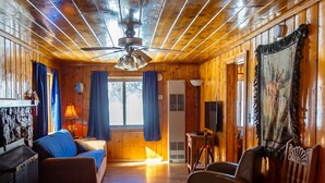 Ein gemütliches Blockhaus-Interieur mit Holzwänden, einem Deckenventilator, einer Couch, einem Esstisch und einem Fernseher.