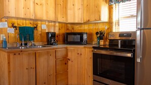 Eine kleine Küche mit Holzausstattung, einem Edelstahl-Kühlschrank, einer Mikrowelle, einer Kaffeemaschine und einem Herd.