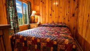 A wooden-paneled room with a bed, a nightstand, a lamp, and a window with curtains. - Located by the River facing the Mountains (Red River)