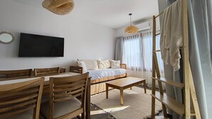 A modern living room with a sofa, wooden chairs, a coffee table, a TV, and a large window with curtains. - Buena Vid by Chadel Management (Cafayate)