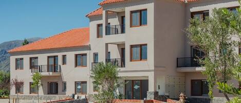 A modern multi-story residential building with a tiled roof, balconies, and a paved courtyard.