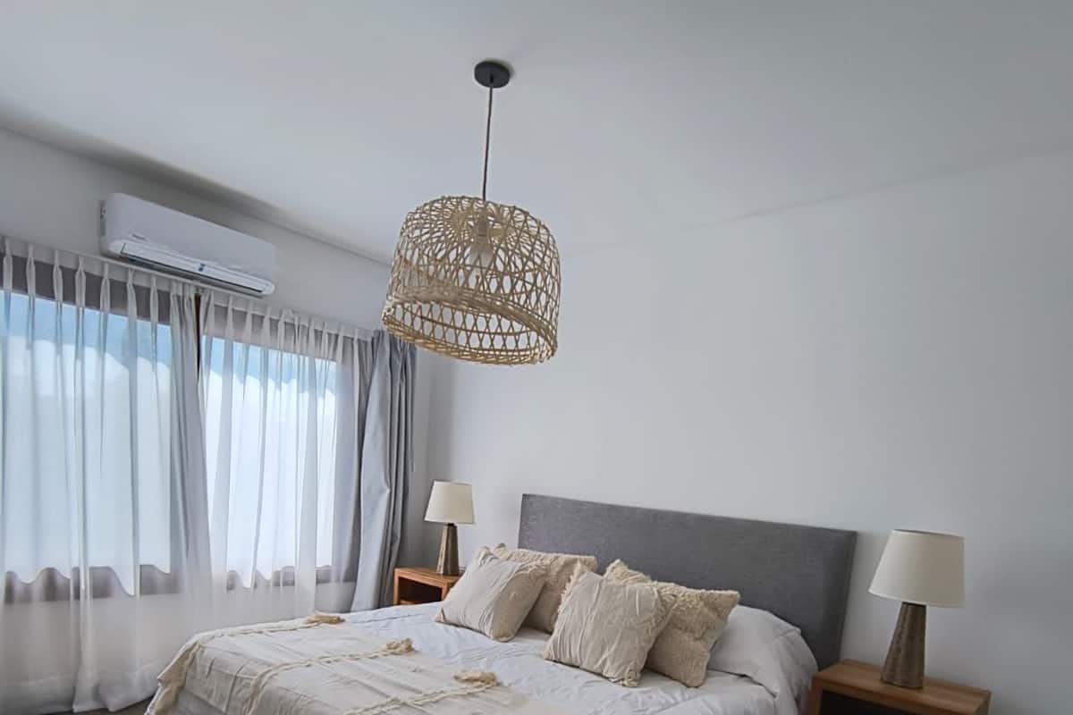 Quarto com uma cama grande, duas mesas de cabeceira, luminária pendente e janela com cortinas.