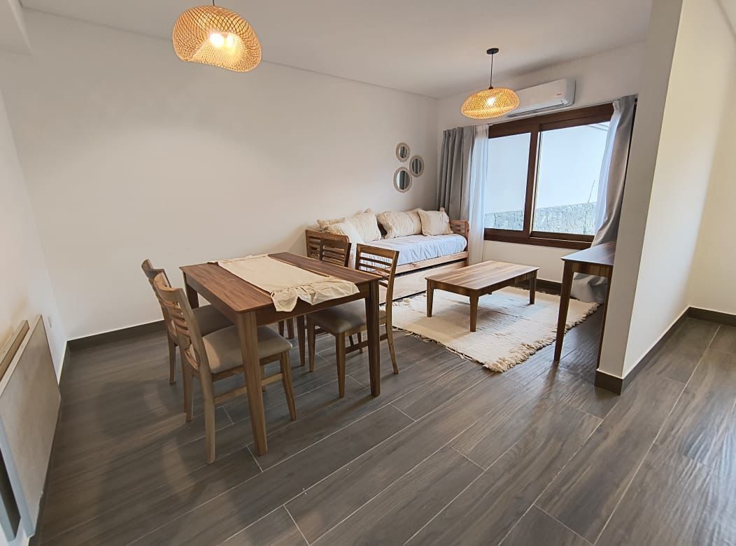A compact living space with a dining area, a sofa bed, and a large window providing natural light.