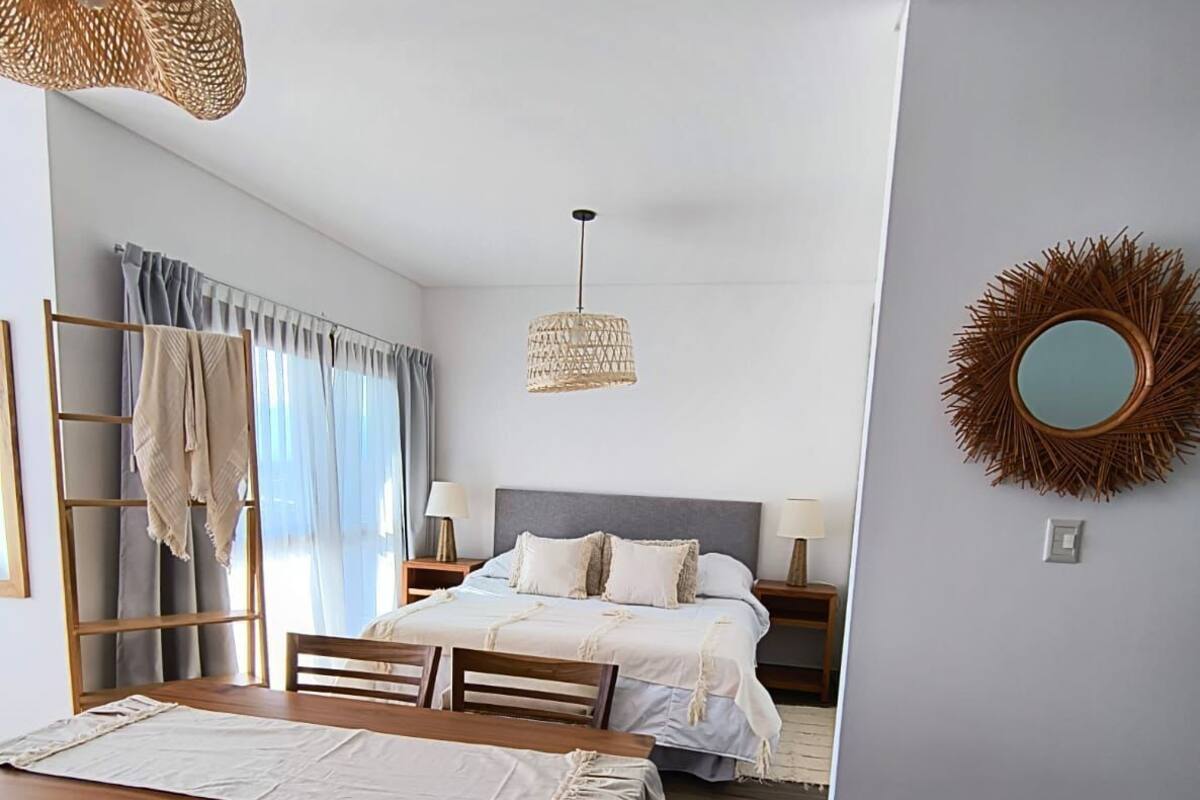 Quarto moderno com cama, mesas de cabeceira, luminária pendente e espelho na parede.