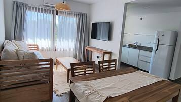 Una sala de estar moderna y bien iluminada con una mesa de comedor de madera, un sofá y un televisor montado en la pared.