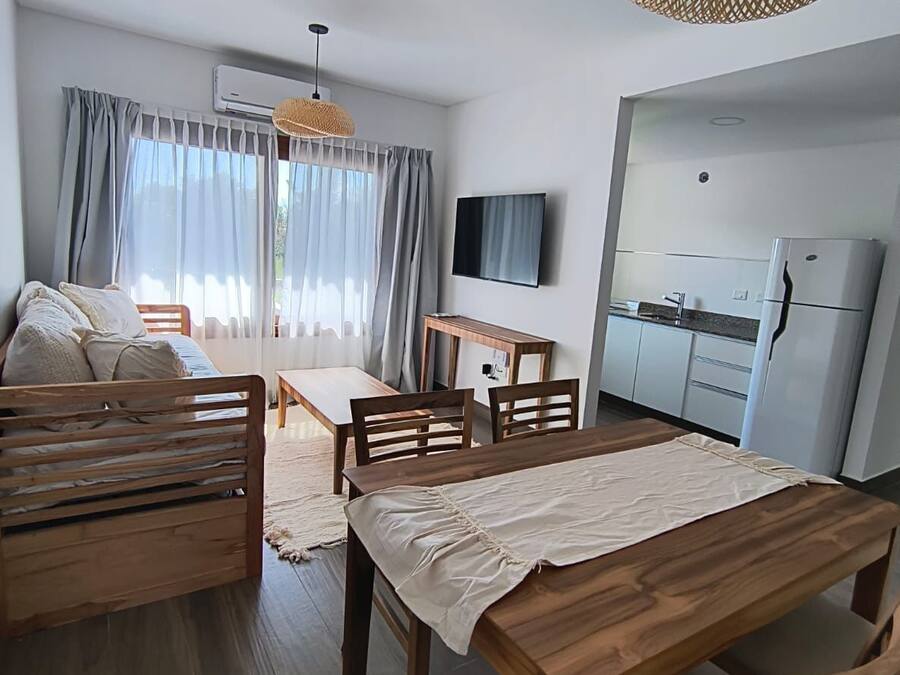 Una sala de estar moderna y bien iluminada con una mesa de comedor de madera, un sofá y un televisor montado en la pared.