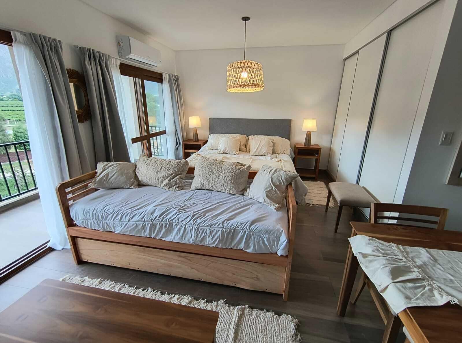 Une chambre moderne avec un grand lit, des tables de chevet, un luminaire suspendu et une vue sur la verdure.