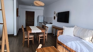 A compact room with a wooden bed, a dining table with chairs, a kitchenette, and a television on the wall. - Buena Vid by Chadel Management (Cafayate)