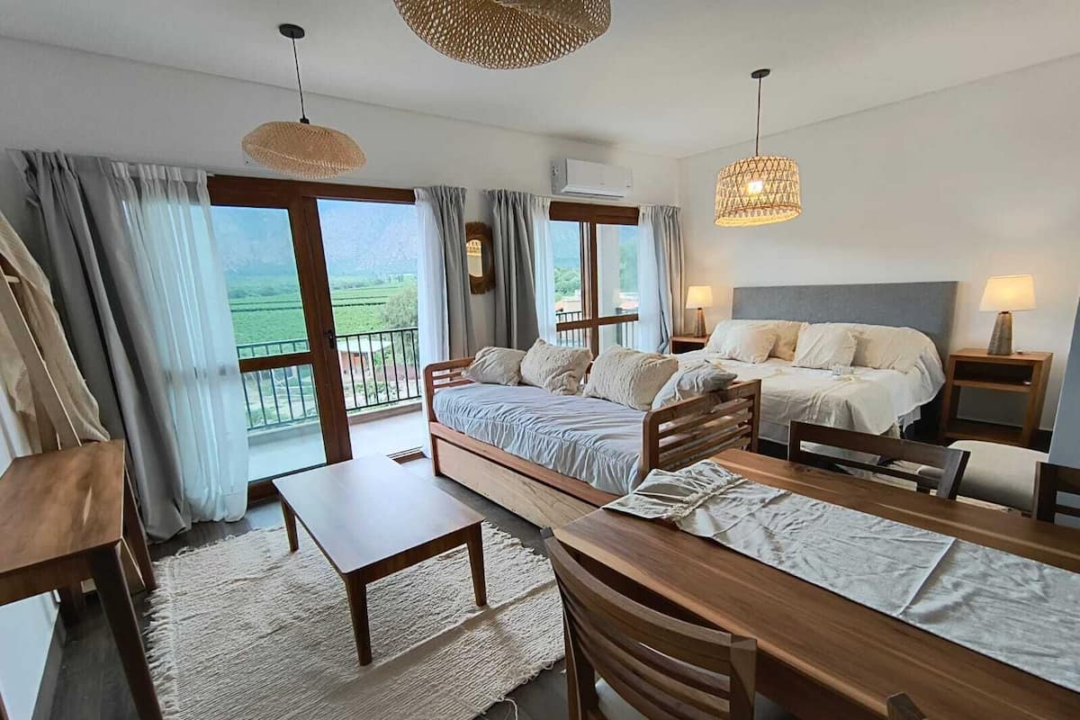 Quarto com uma cama grande, uma cama menor, uma mesa de jantar e uma varanda com vista para o campo.