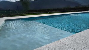 A swimming pool with clear blue water, surrounded by a white deck. In the background, there are mountains and a partly cloudy sky. - Buena Vid by Chadel Management (Cafayate)