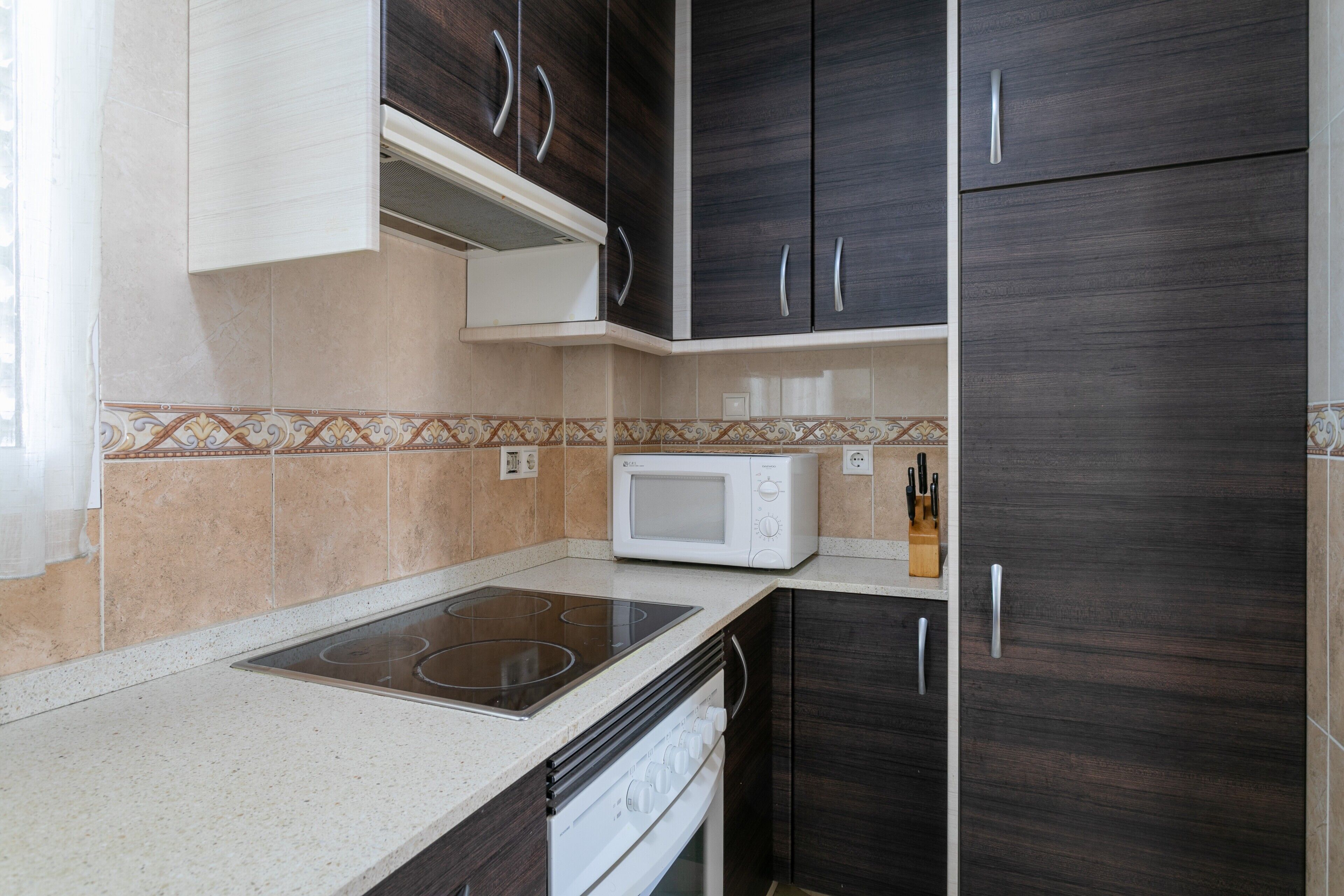 A kitchen with a microwave, stove, and dark wooden cabinets.
