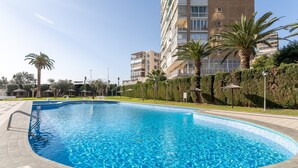 A swimming pool surrounded by a landscaped area with palm trees and a multi-story building in the background. - Apartment 'Urbanización Las Torres' with Sea View, Wi-Fi and Air Conditioning (Alacant)