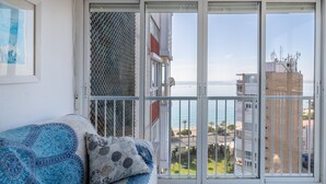 A balcony with a view of the sea and buildings, a sofa with patterned cushions, and a window with a mesh screen. - Apartment 'Urbanización Las Torres' with Sea View, Wi-Fi and Air Conditioning (Alacant)