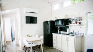 A compact kitchen with white cabinetry, a black refrigerator, a microwave, and a coffee machine. There is a small dining area with a white table and chairs. - Lakefront Two Bedroom Cabin #32 (Charlotte)