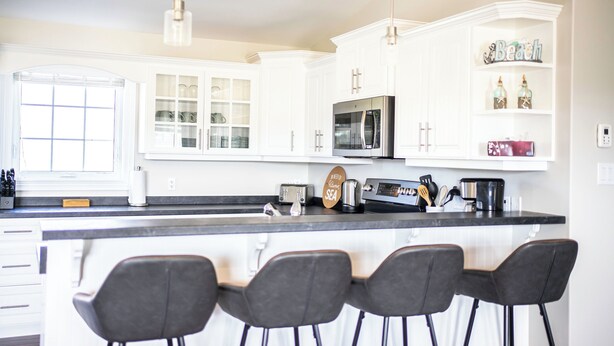 A kitchen with white cabinetry, a central island with bar stools, a microwave, and a coffee maker.