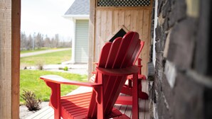 A red Adirondack chair on a wooden deck with a view of a house and a grassy yard.