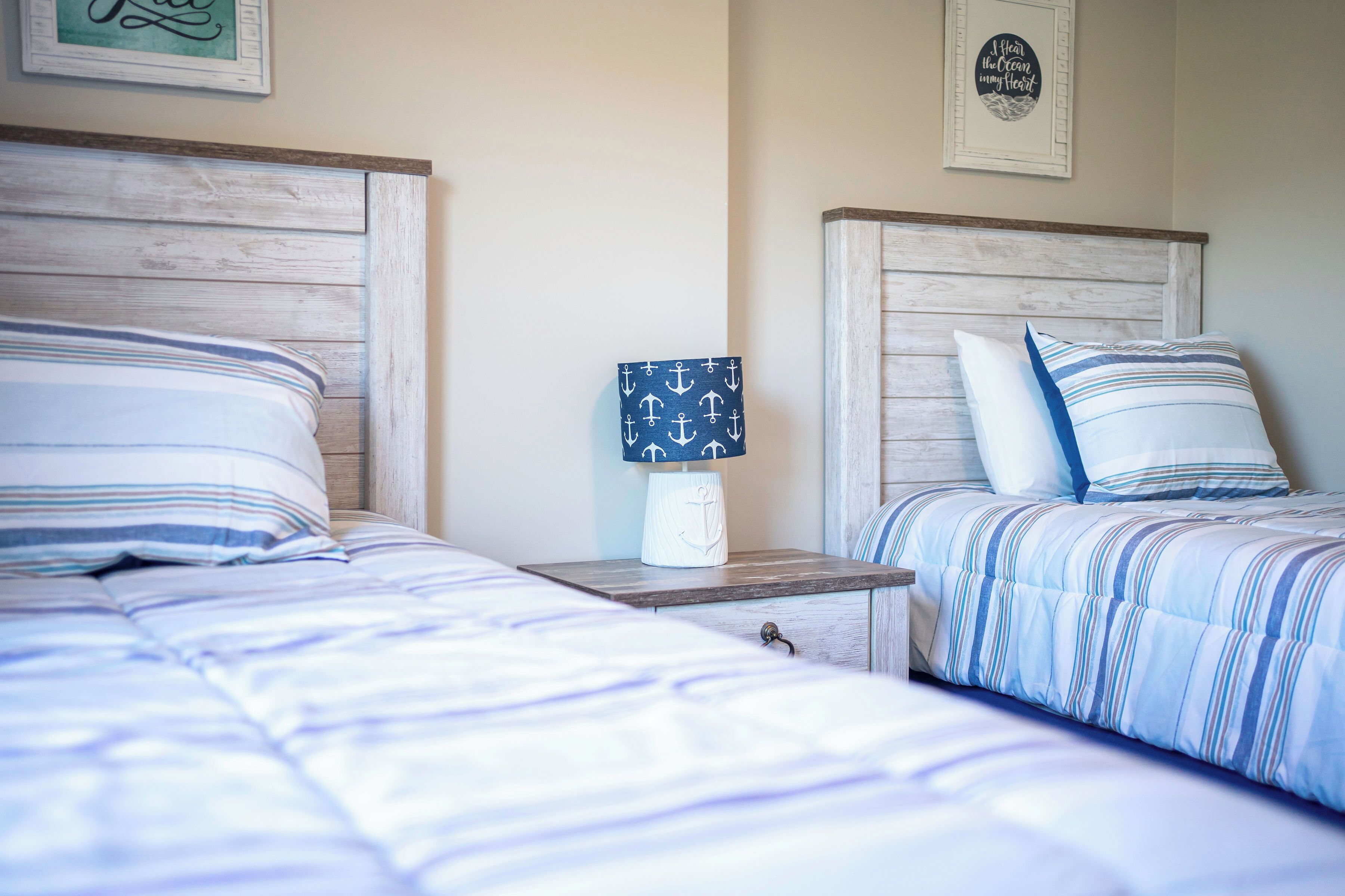Uma cama de casal com roupa de cama listrada, uma mesinha de cabeceira com abajur e uma parede decorada com tema náutico.