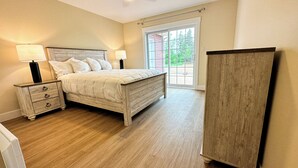 Een slaapkamer met een bed, nachtkastjes, een dressoir en een schuifdeur naar buiten.