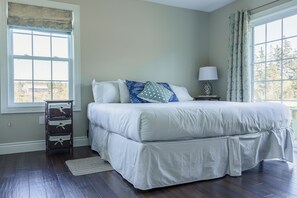 Une chambre à coucher avec un grand lit, une table de chevet, une lampe, une fenêtre avec des rideaux et un plancher en bois.