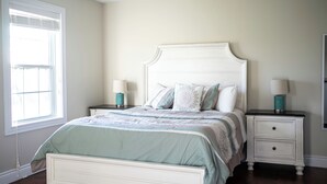 A bedroom with a bed, two bedside tables, a window, and a nightstand.