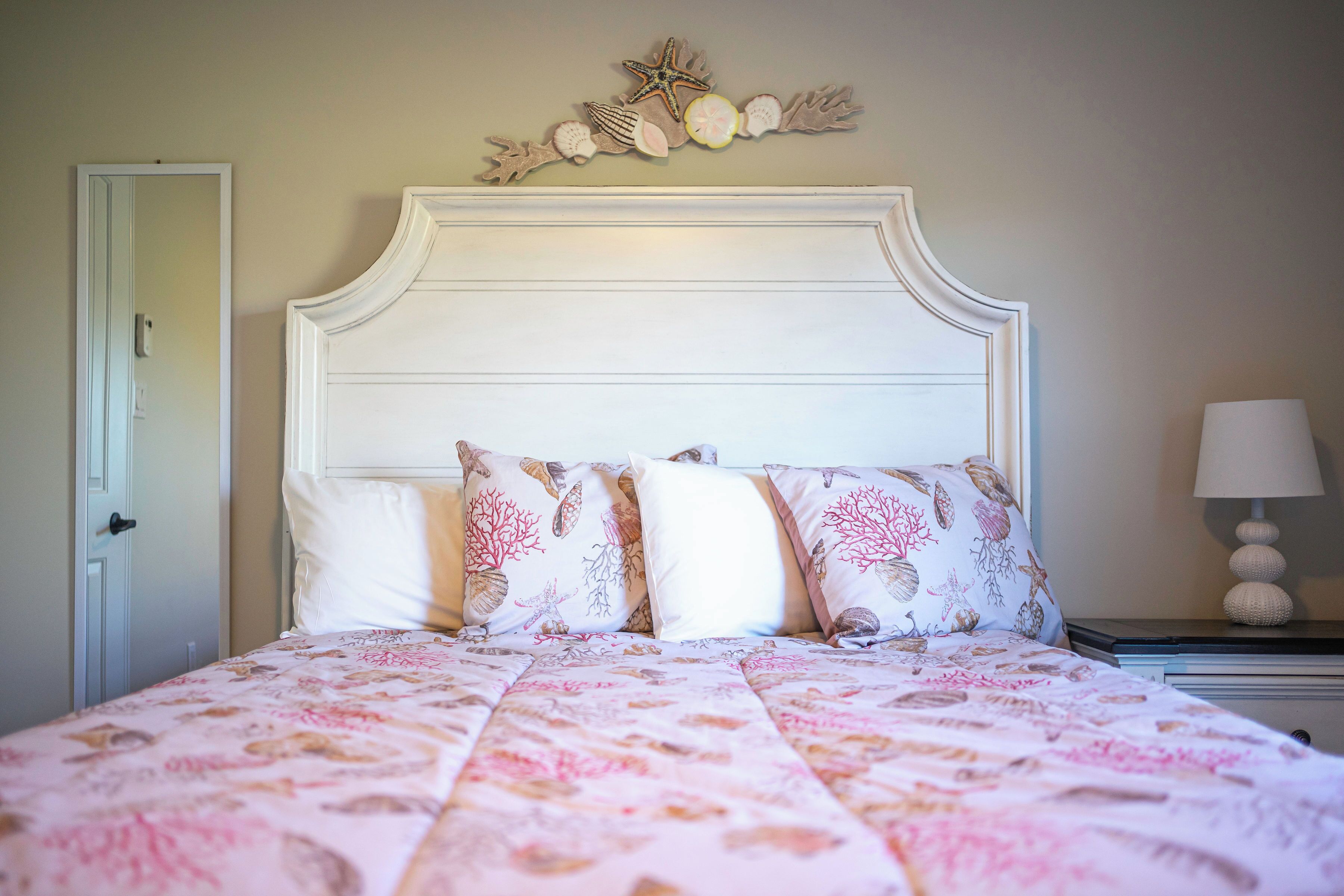Una cama con ropa de cama floral, un cabecero decorativo y una mesita de noche con lámpara.